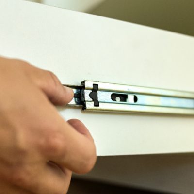 Close up of carpenter hands installing wooden drawer on sliding skids in contemporary cupboard cabinet.