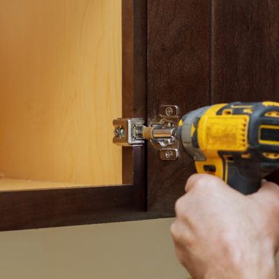 Installation of kitchen. Workman fixes a hinge to a kitchen cabinet.