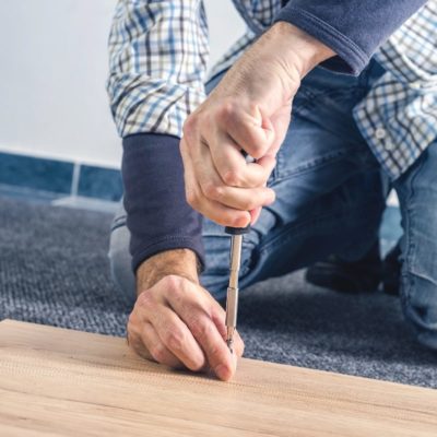 Man assembling furniture at home on the floor, hand with screwdriver