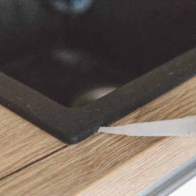 Man sealing kitchen sink joint between sink and countertop by silicone sealant.